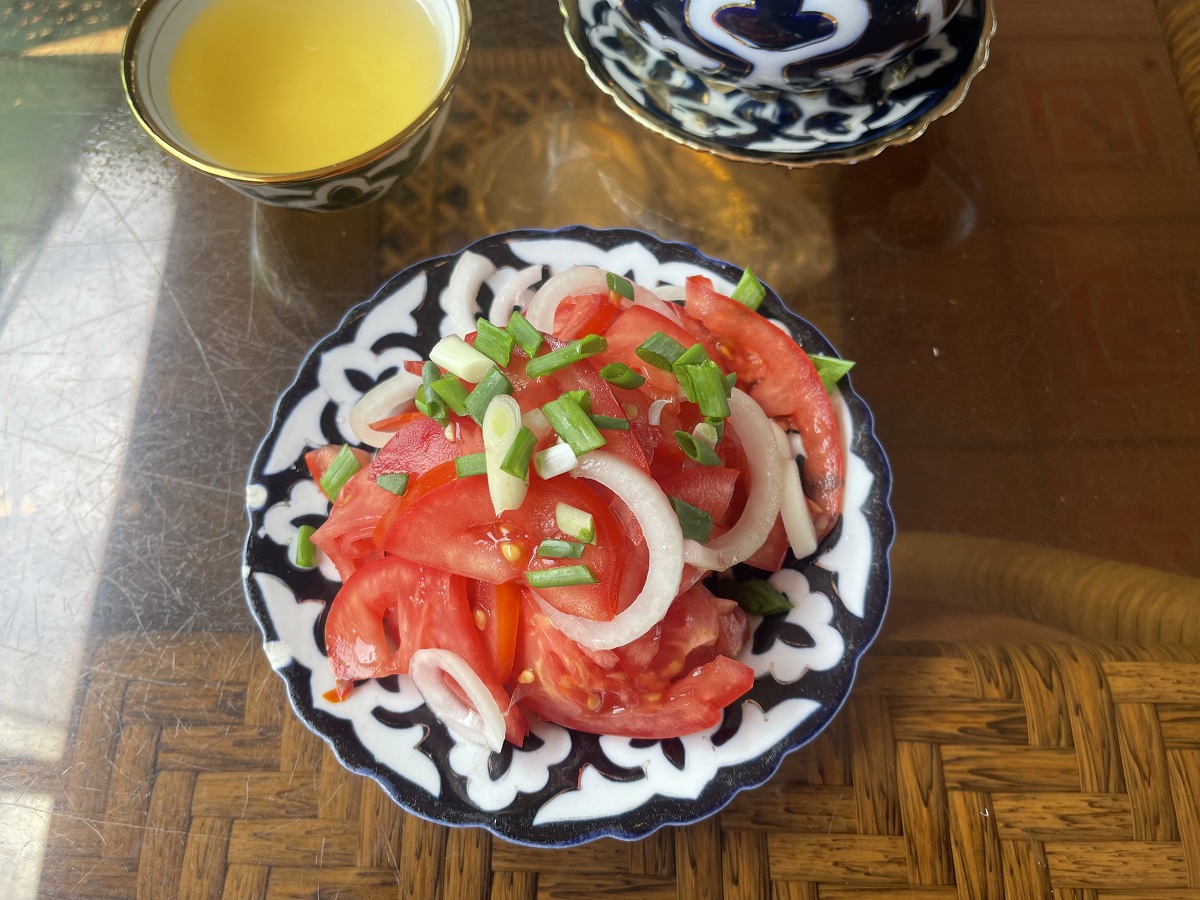 A vibrant plate of achichuk salad, made with fresh tomatoes, onions, and green herbs, served alongside a cup of lemon tea in Uzbekistan. This dish is a popular vegetarian option in Uzbek cuisine.