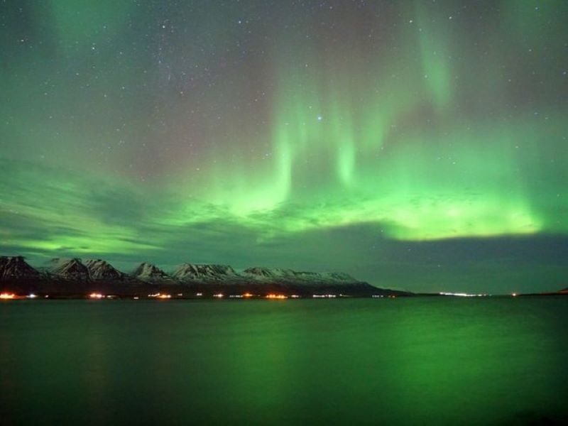 northern lights over a water body flanked by mountains in iceland