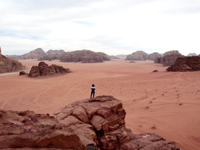 woman standing atop a rock looking into the distance in the jordanian desert