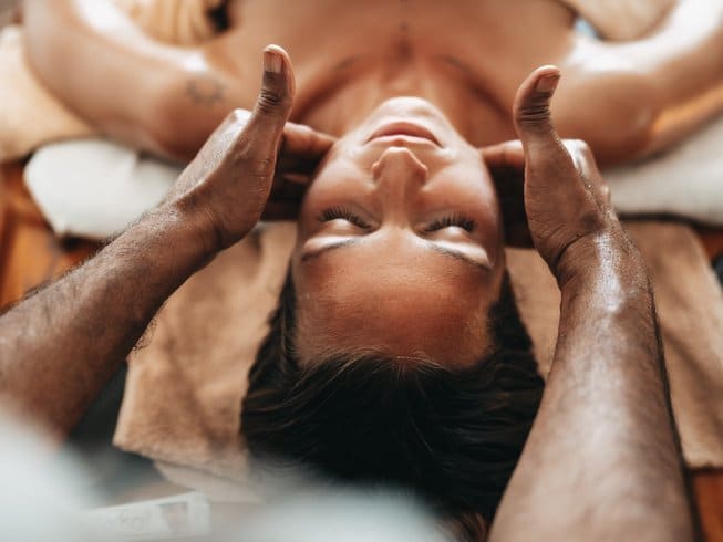 woman laying down with two hands massaging her jaw