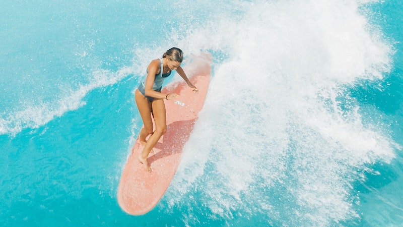 woman on a pink surf board learning to surf in Bali on a retreat