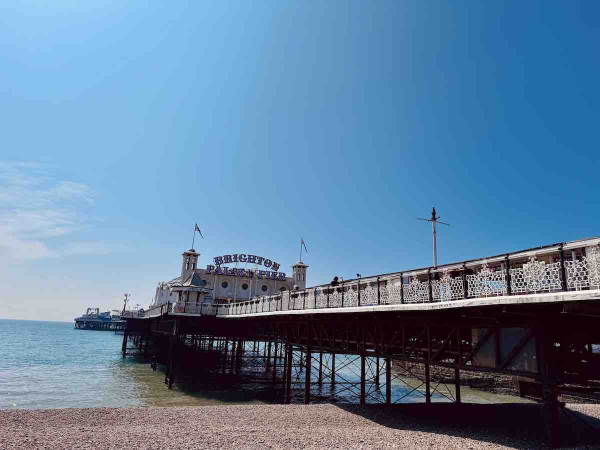 Brighton Palace Pier extending over the sea on a sunny day, with clear blue skies and calm waters along the pebble beach.