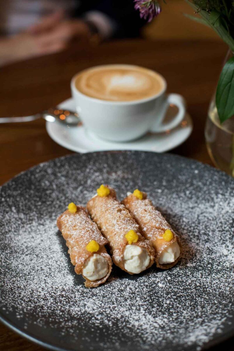 woman eating traditional cannoli in Sicily on a black plate dusted with powdered sugar