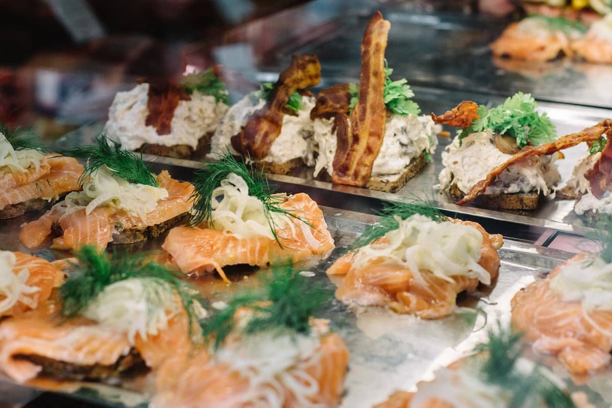 A close-up of traditional Danish smørrebrød, featuring open-faced sandwiches with fresh salmon, dill, pickled onions, and creamy toppings on rye bread, displayed on a serving tray in Copenhagen.