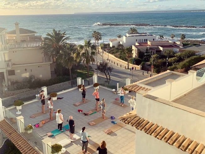 group of people on a Mallorca yoga retreat standing in mountain pose on an outdoor deck in Colonia de Sant Jordi
