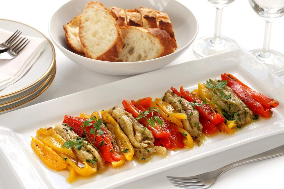 Escalivada, a traditional Spanish vegan dish featuring roasted red and yellow peppers, eggplant, and onions, served with fresh bread.