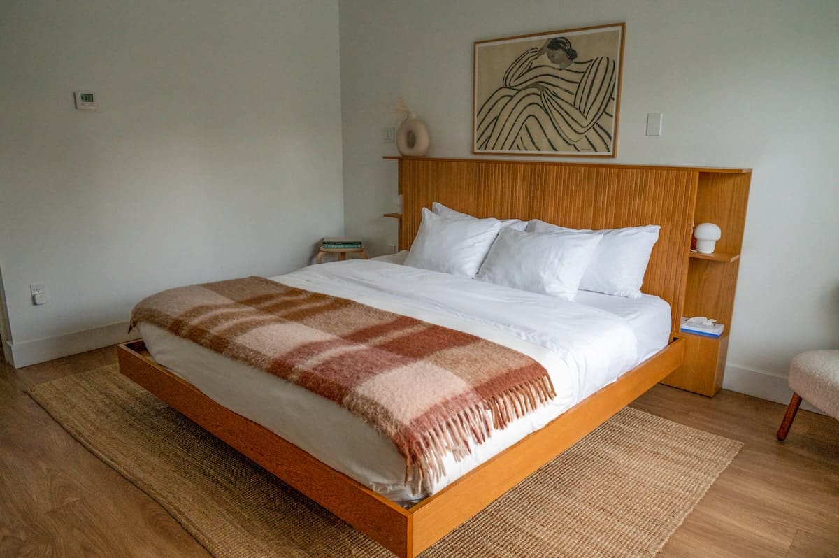 A cozy, minimalist room at The Evangeline Inn in Grand Pré, featuring a comfortable bed with a plaid throw blanket, modern wooden furnishings, and simple artwork on the wall.