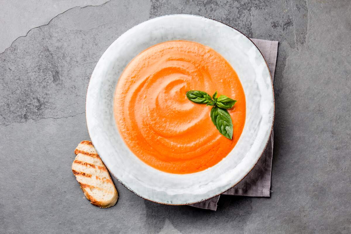 Gazpacho, a classic Spanish vegan soup made from blended tomatoes, cucumbers, and peppers, garnished with a basil leaf.