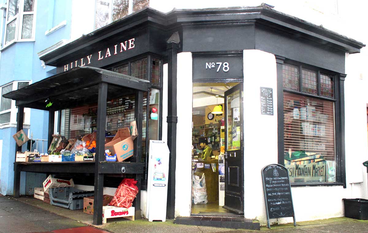 Exterior of Hilly Laine, a small vegan-friendly grocery shop in Brighton, with fresh produce boxes displayed outside and the front door open to a cozy interior.