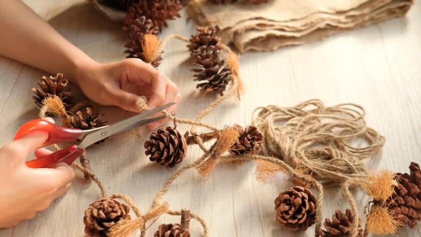 person making their own holiday decorations using string and pinecones