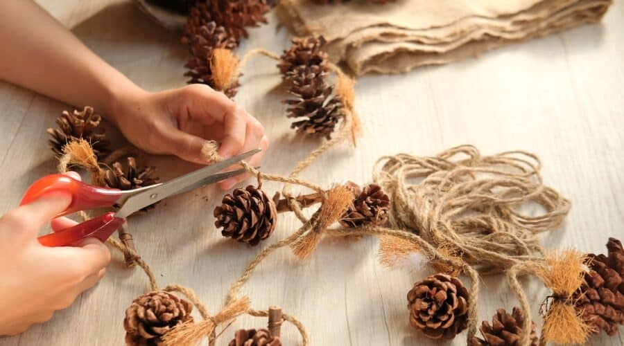 person making their own holiday decorations using string and pinecones