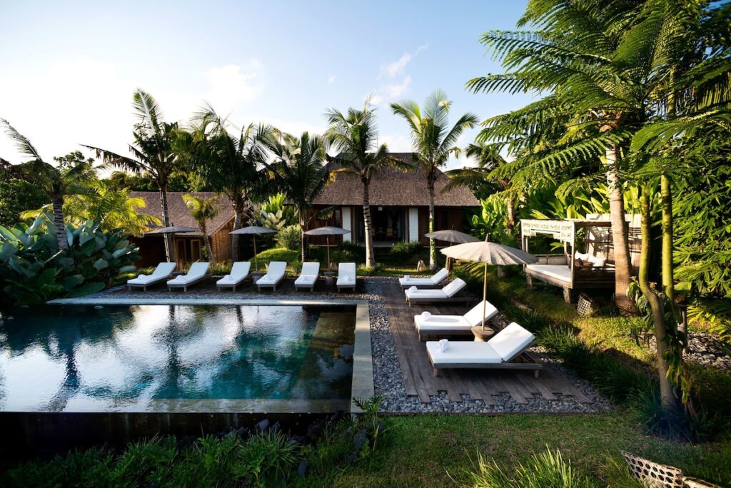 pool surrounded by white lounge chairs and palm trees at the Kalapa Resort and Yoga Retreat in Canggu, Bali
