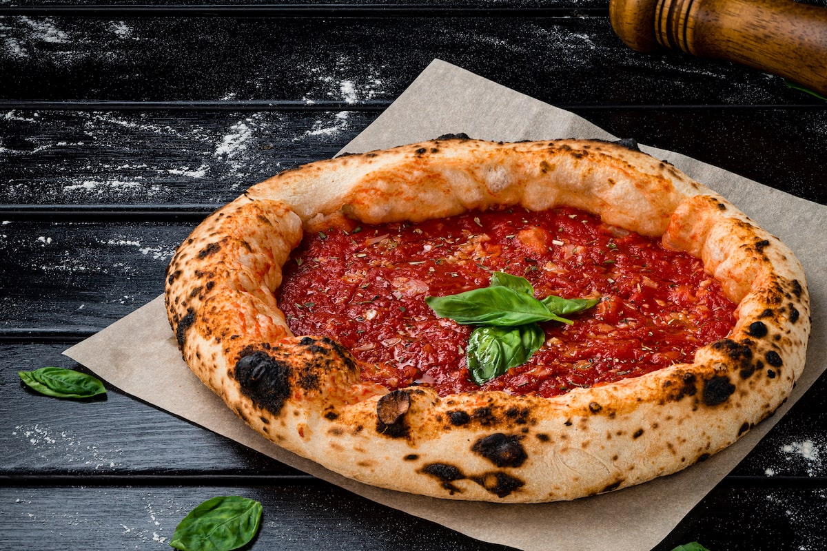 Neapolitan-style pizza marinara topped with tomato sauce, garlic, oregano, and fresh basil, served on parchment paper over a dark rustic background.