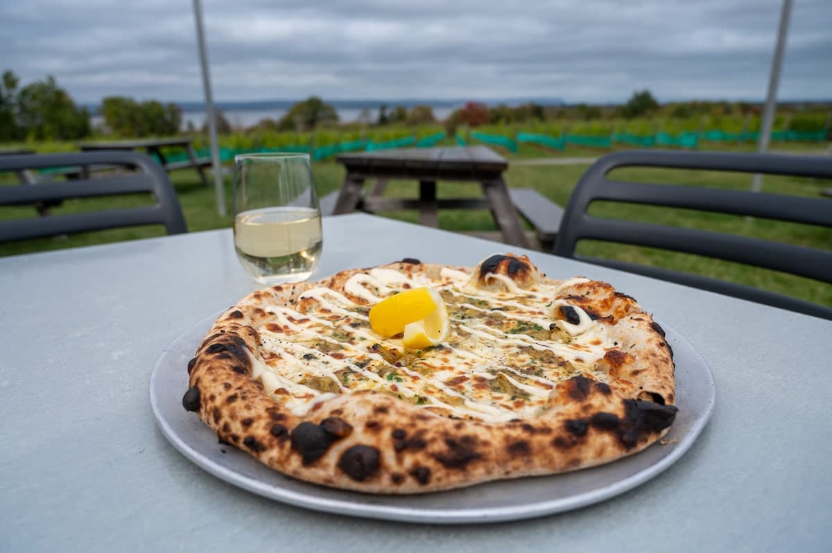 Pairing Tidal Bay L'Acadie Blanc with a PEI clam pizza at Lightfoot & Wolfville Vineyard in Wolfville, Nova Scotia, showcasing local wine and cuisine.