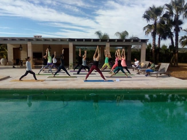 group of people on a Mallorca retreat doing yoga around a swimming pool in S'Illot