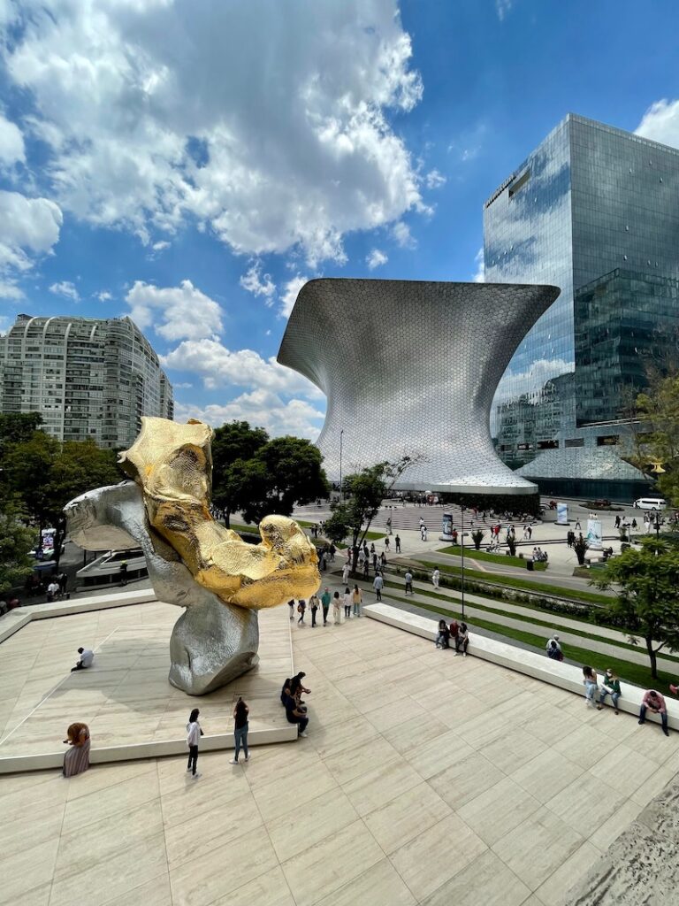 woman gazing at a giant silver and bronze sculpture while exploring the Mexico City art scene