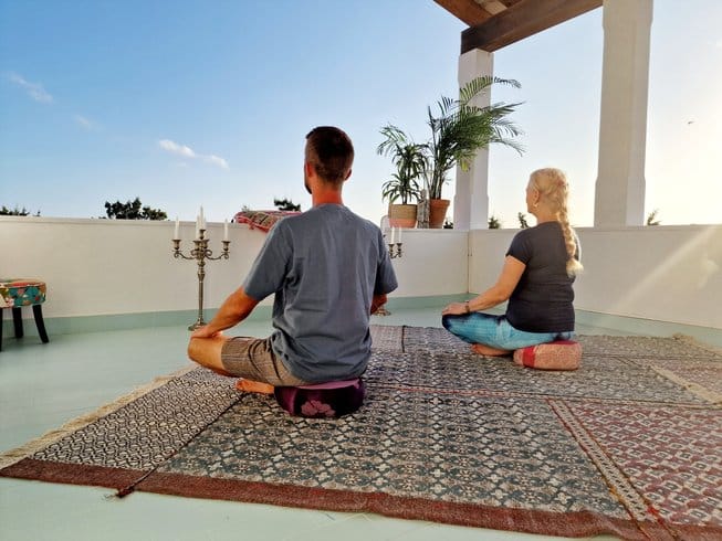 two people sitting on pillows meditating on an outdoor deck during a Mallorca retreat 