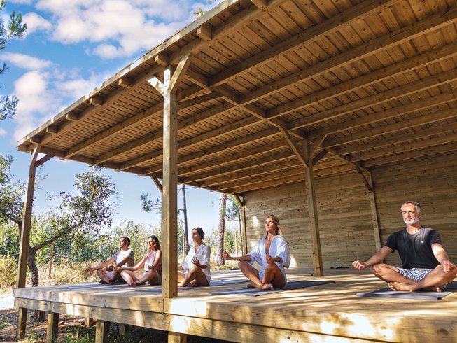 five people sitting in lotus pose on an outdoor deck during a wine and yoga retreat in Costa Vicentina, Portugal