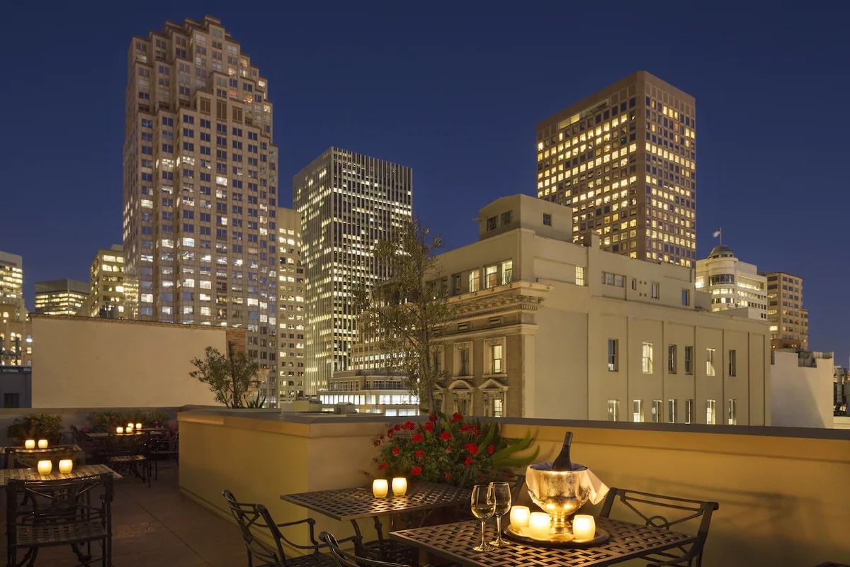 A rooftop dining area at the vegan Orchard Garden Hotel in San Francisco, featuring candlelit tables and a stunning view of the city skyline illuminated at night.