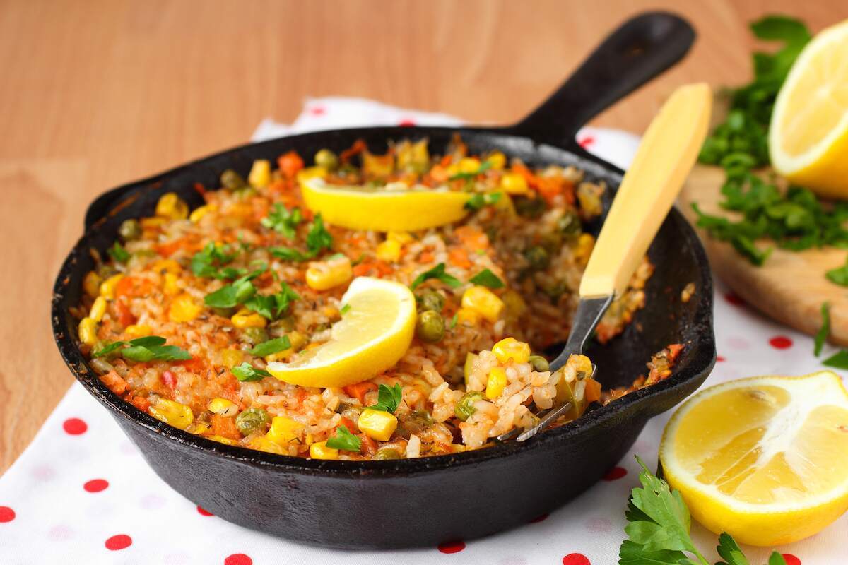 Paella de Verduras, a Spanish vegan dish featuring a colorful vegetable paella with rice, peas, corn, and bell peppers, garnished with lemon wedges.