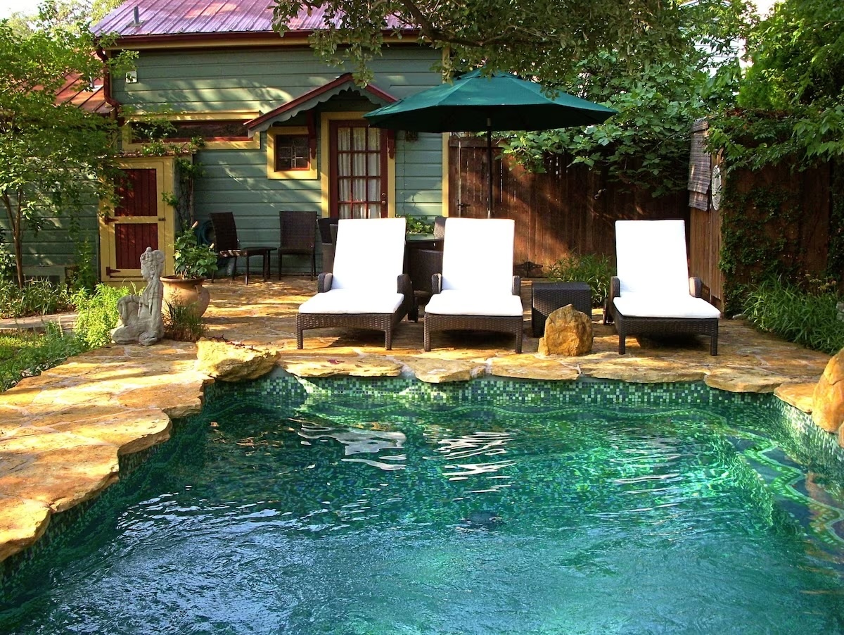 Charming pool area at Park Lane Guest House eco-hotel in Austin, Texas, featuring comfortable lounge chairs, a stone poolside, and a serene garden setting.