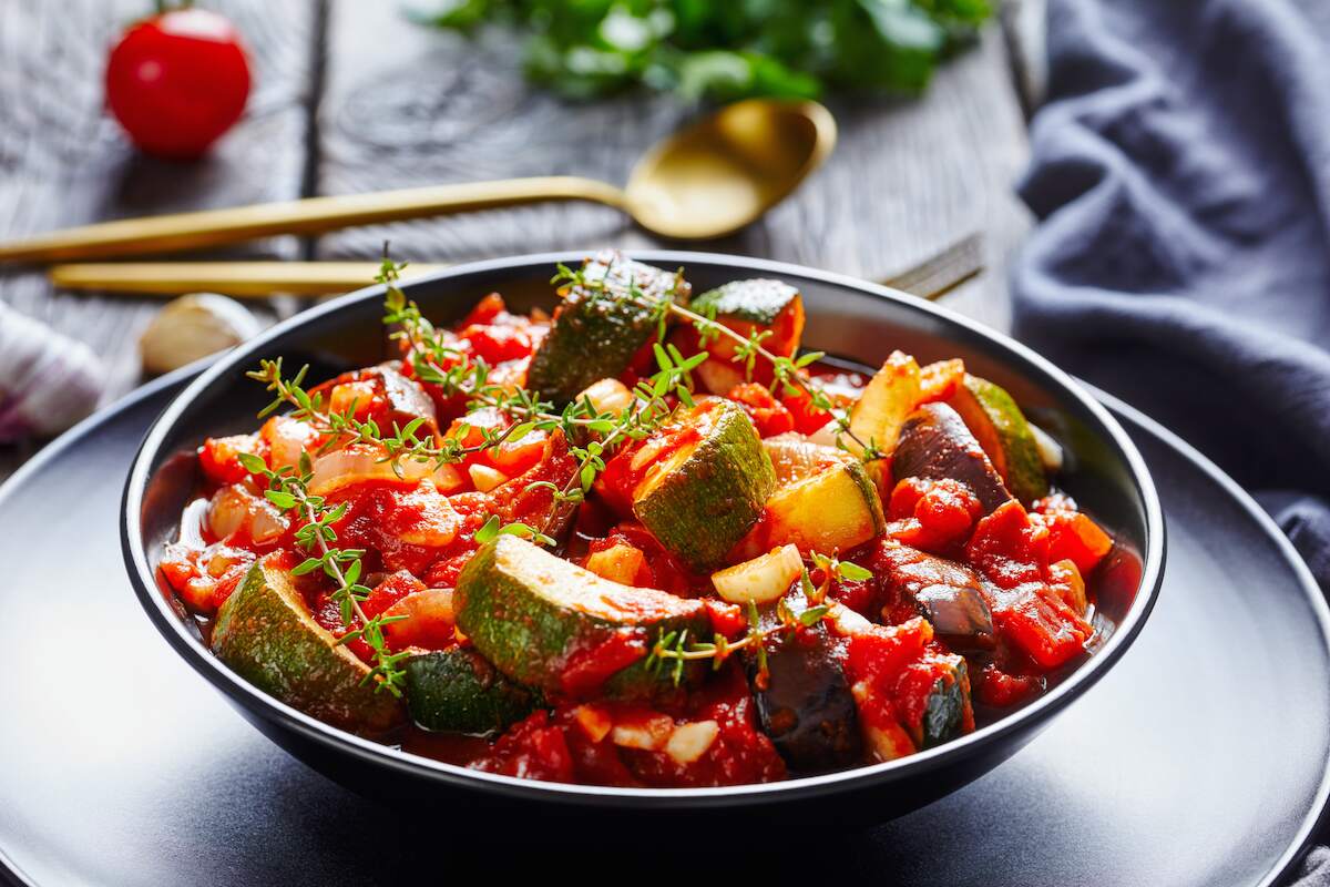 Pisto Manchego, a Spanish vegan dish featuring a hearty mix of sautéed zucchini, eggplant, tomatoes, and onions, garnished with fresh herbs.