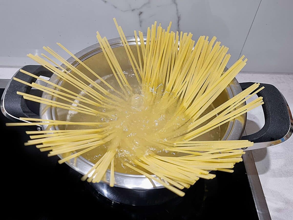 Uncooked linguine pasta fanned out in a pot of boiling water, gradually softening and sinking into the water on a stovetop.