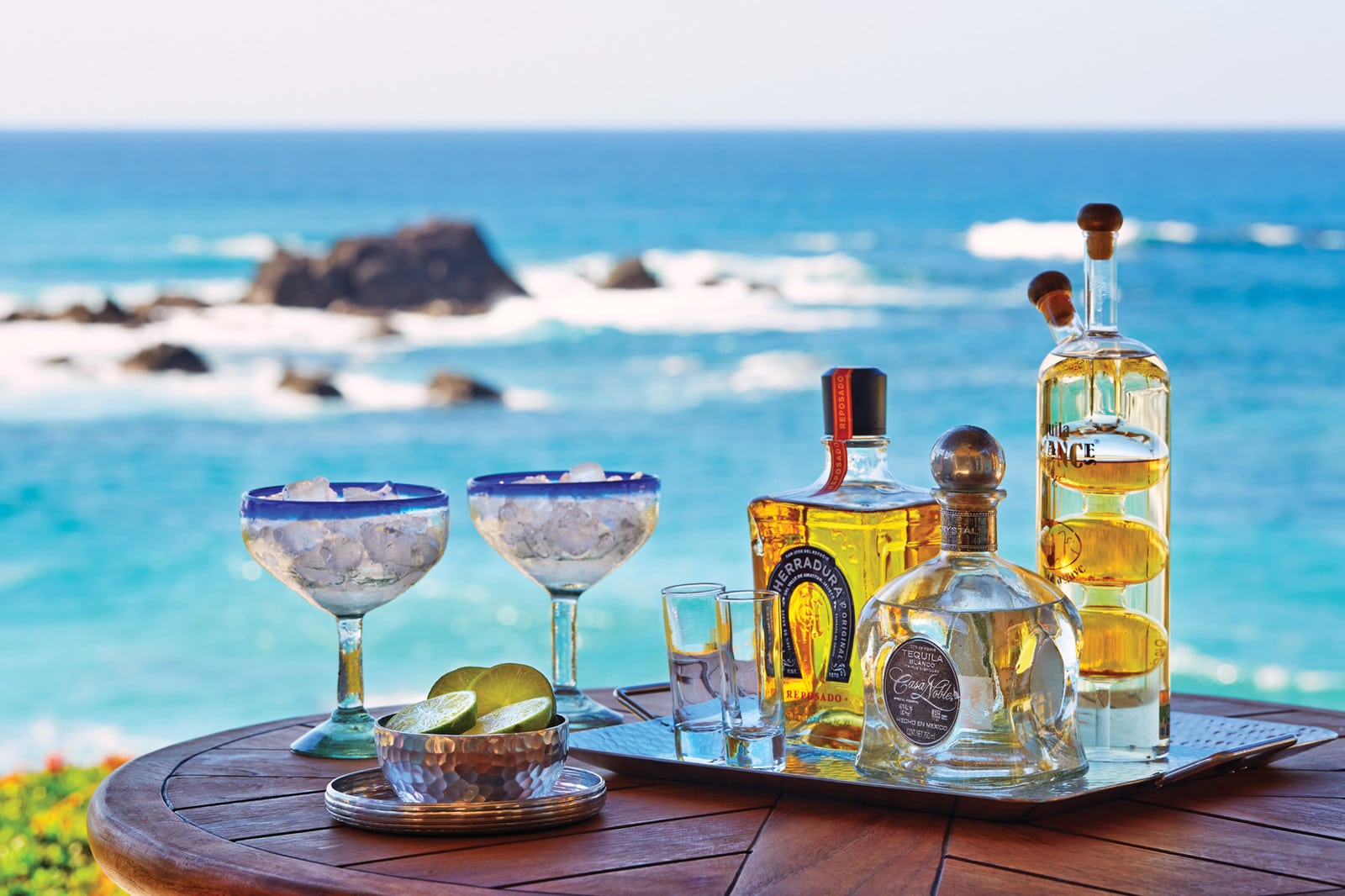 table set with bottles of tequila and bowls of lime with the blue sea behind it in Puerto Vallarta, Mexico