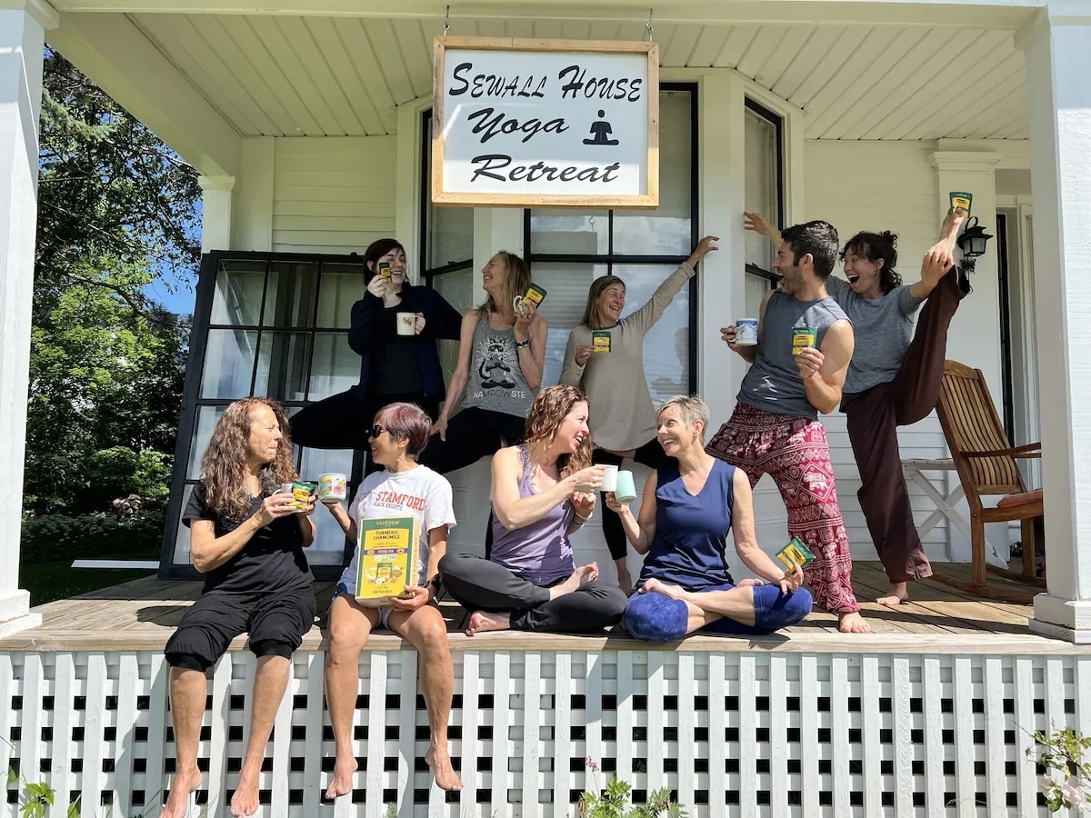 Group of smiling vegan yoga retreat participants enjoying drinks on the porch at Sewall House Yoga Retreat in Island Falls, Maine.