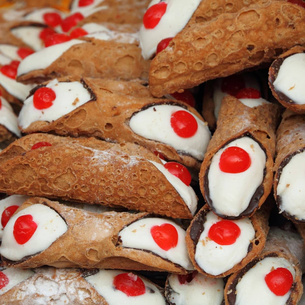 A large plate of chocolate cherry cannoli, featuring crisp shells filled with chocolate cream and adorned with candied cherries on top.