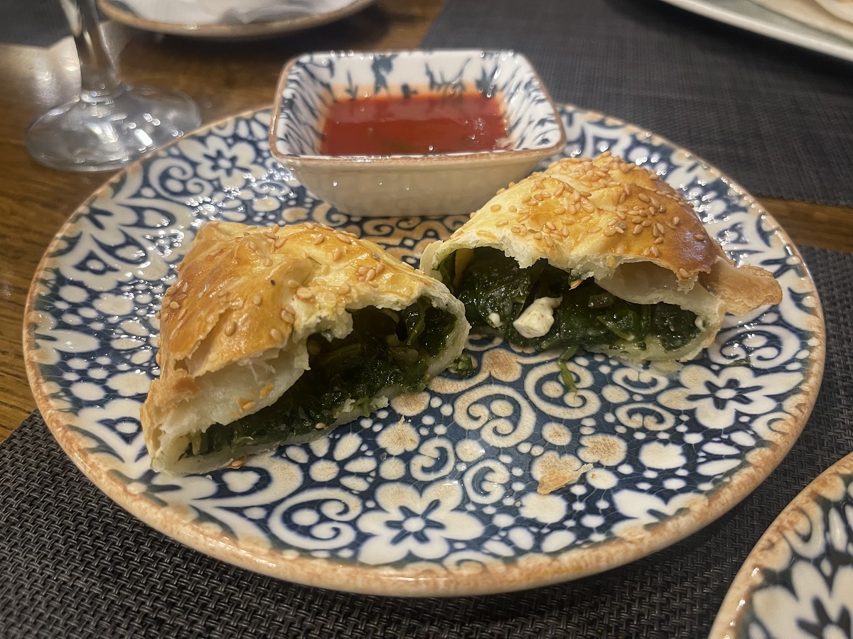 A plate featuring a spinach and feta samosa, cut open to reveal the filling, accompanied by a dish of Uzbek tomato sauce. This vegetarian dish highlights the fusion of flavors in Uzbek cuisine.