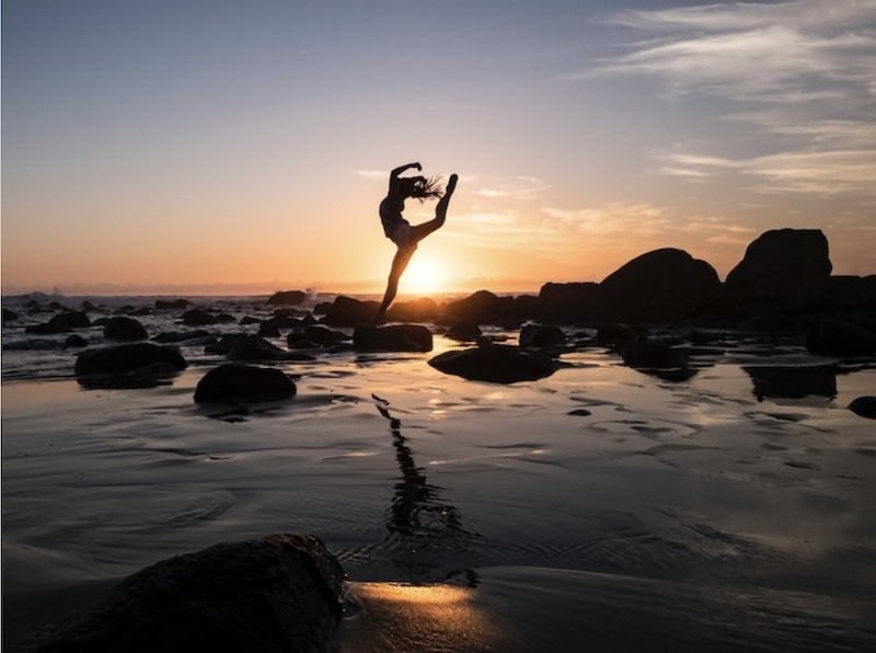 woman doing a yoga pose while jumping in front of a sunset with her reflection shown on the water 