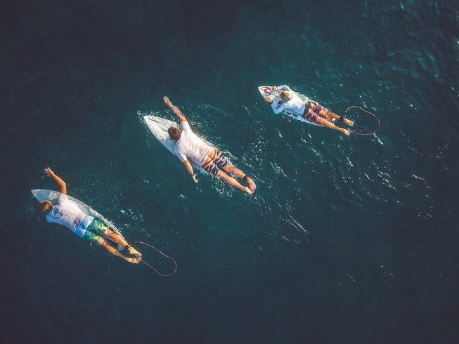three people swimming out to ride a wave during a surfing lesson
