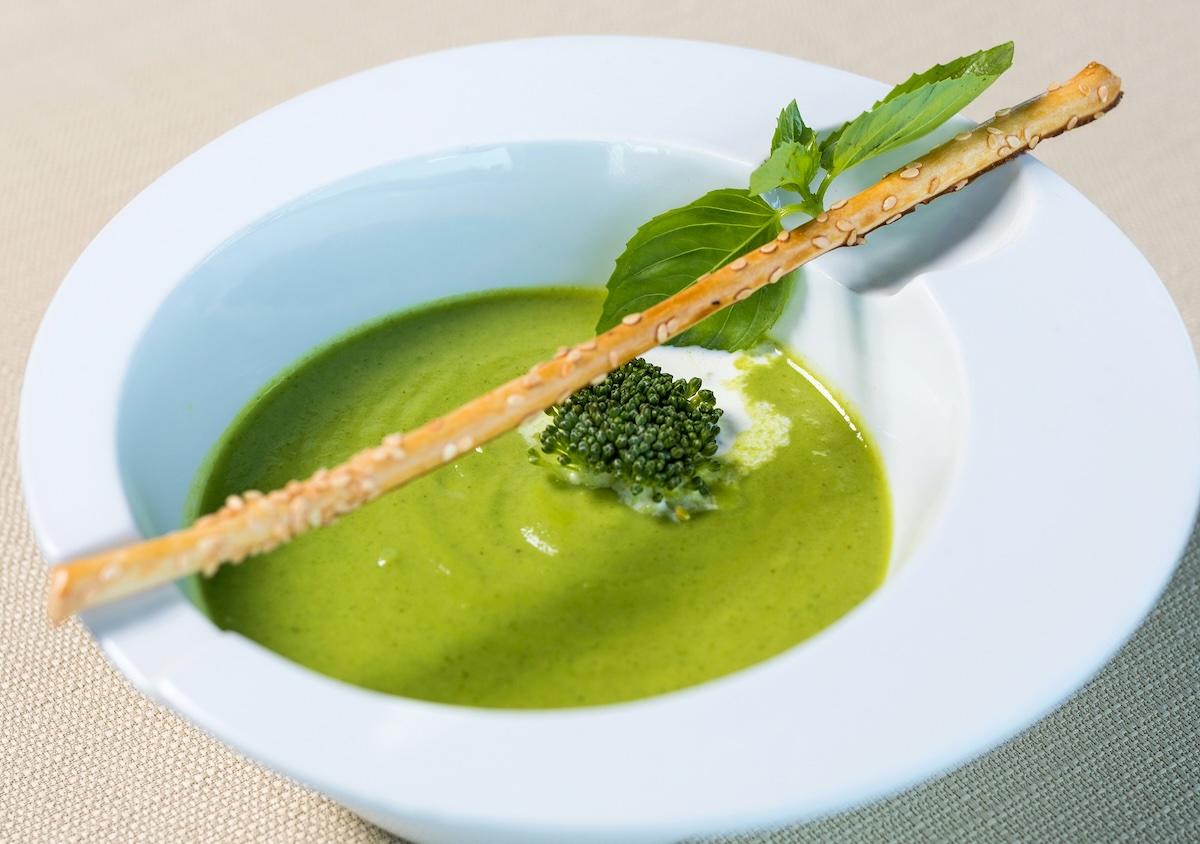 A bowl of green pea soup garnished with a herb and served with a sesame breadstick served at one of the best vegan hotels in the UK, The Clover Mill in Worcestershire.