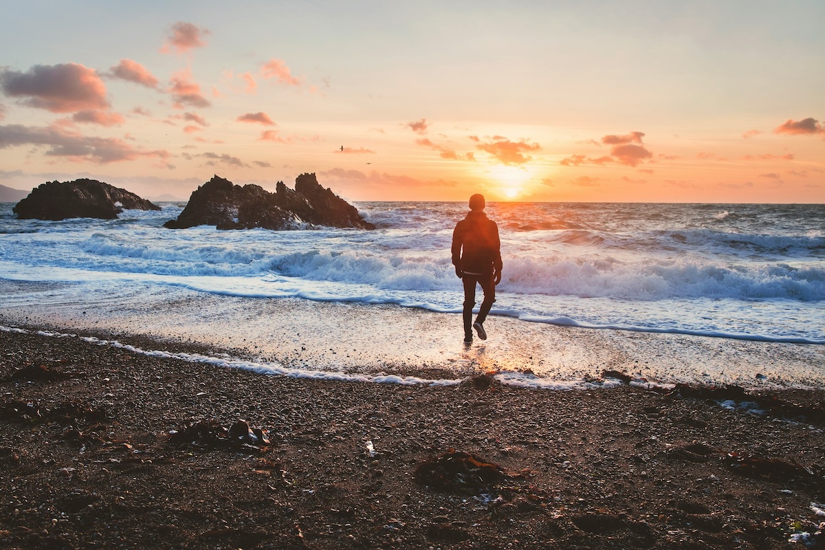 A person standing on stepping stones in a serene beach, surrounded by rocks.