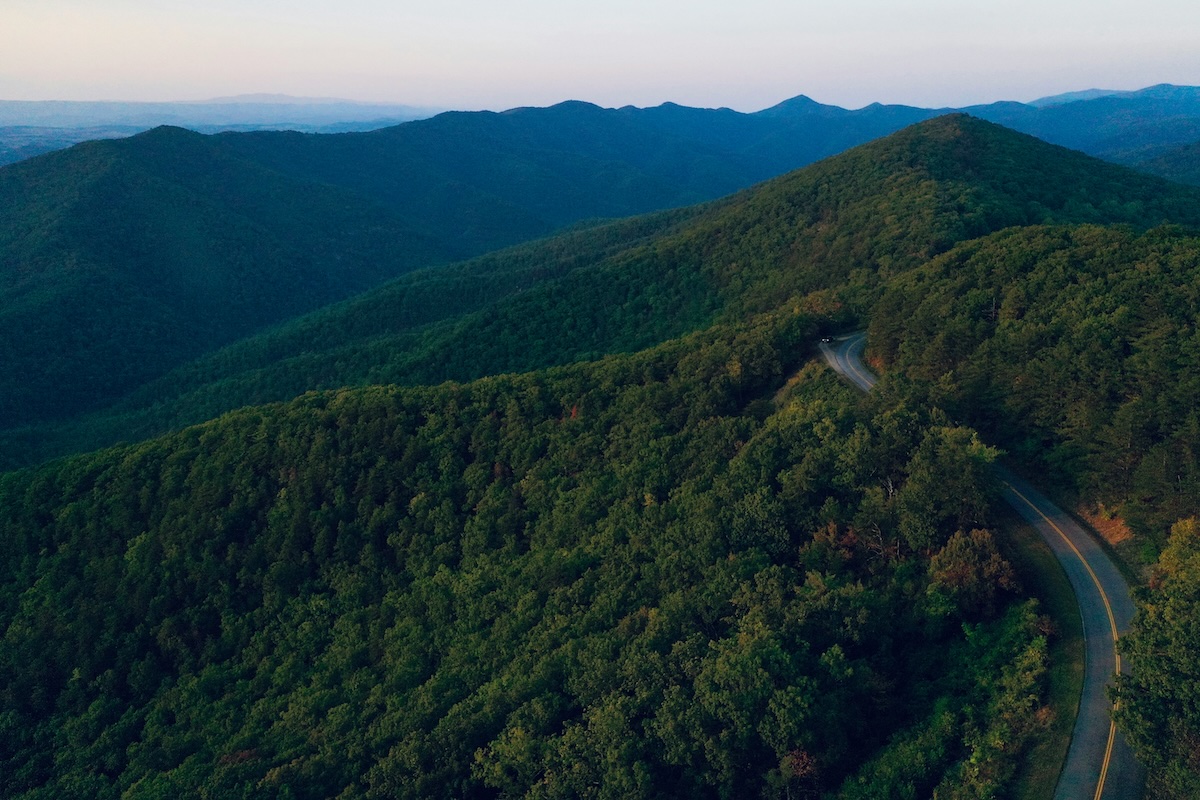 Aerial view of the Blue Ridge Mountains in Virginia, showcasing rolling green peaks and a winding road cutting through the dense forest.