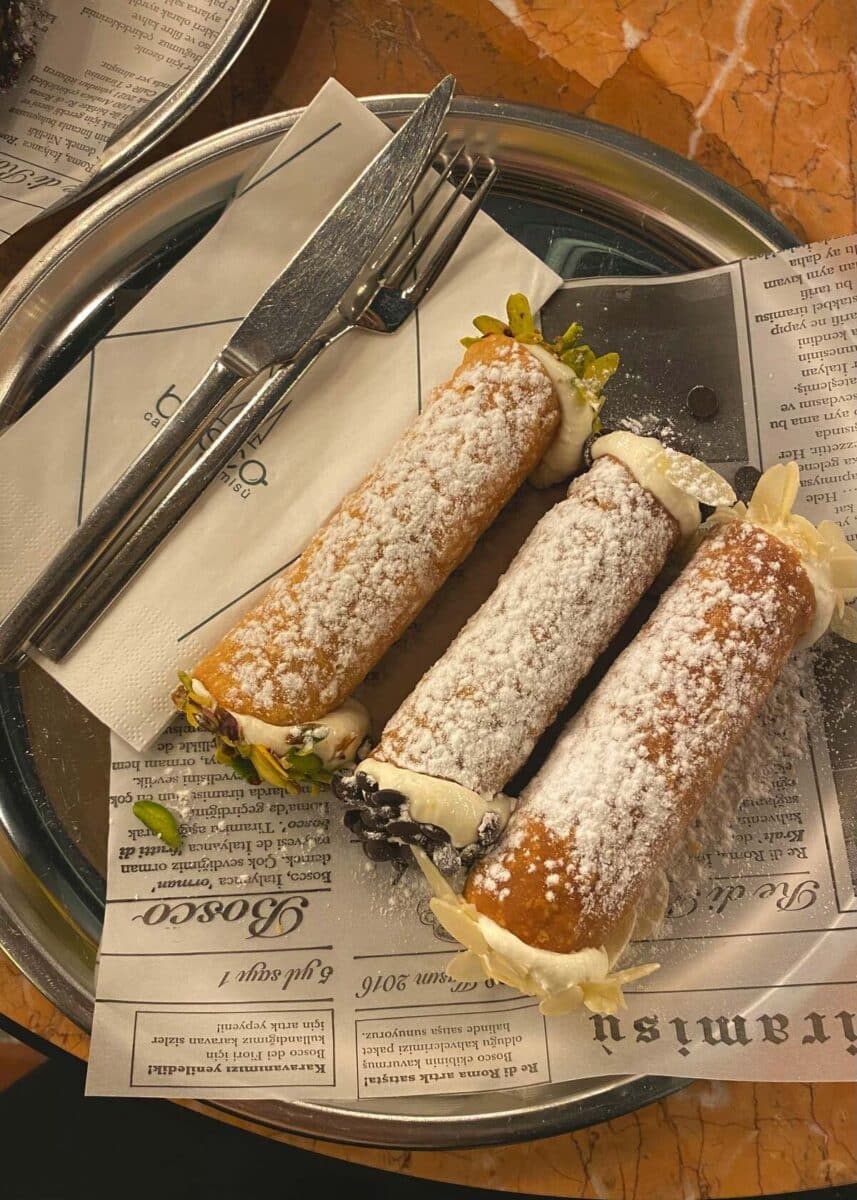 three cannolis on a clear plate from a pasticceria in Sicily