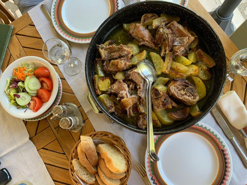 Traditional Croatian peka dish made with lamb and potatoes, accompanied by a seasonal salad and fresh bread