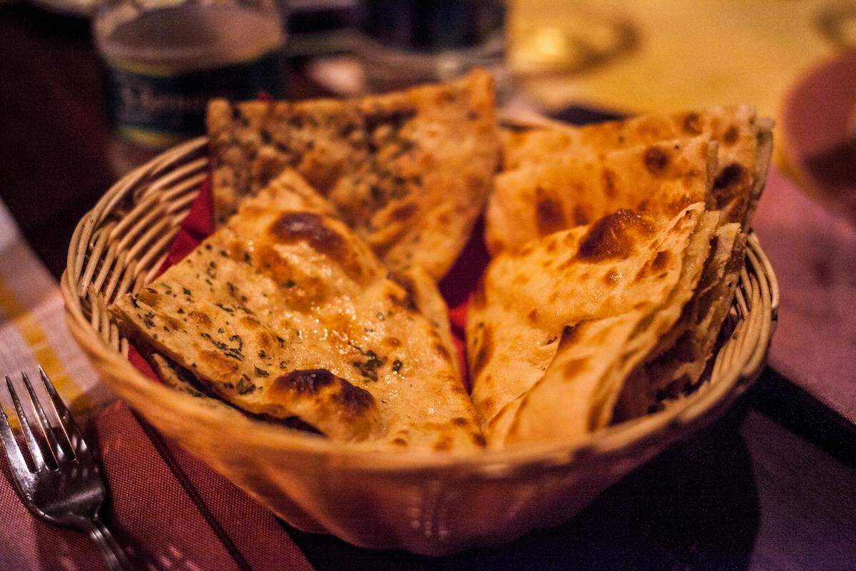 A basket of freshly baked Indian flatbread, a popular vegetarian-friendly food available at local Indian restaurants in Uzbekistan. The flatbread is golden brown and seasoned with herbs, perfect for pairing with various vegetarian dishes.