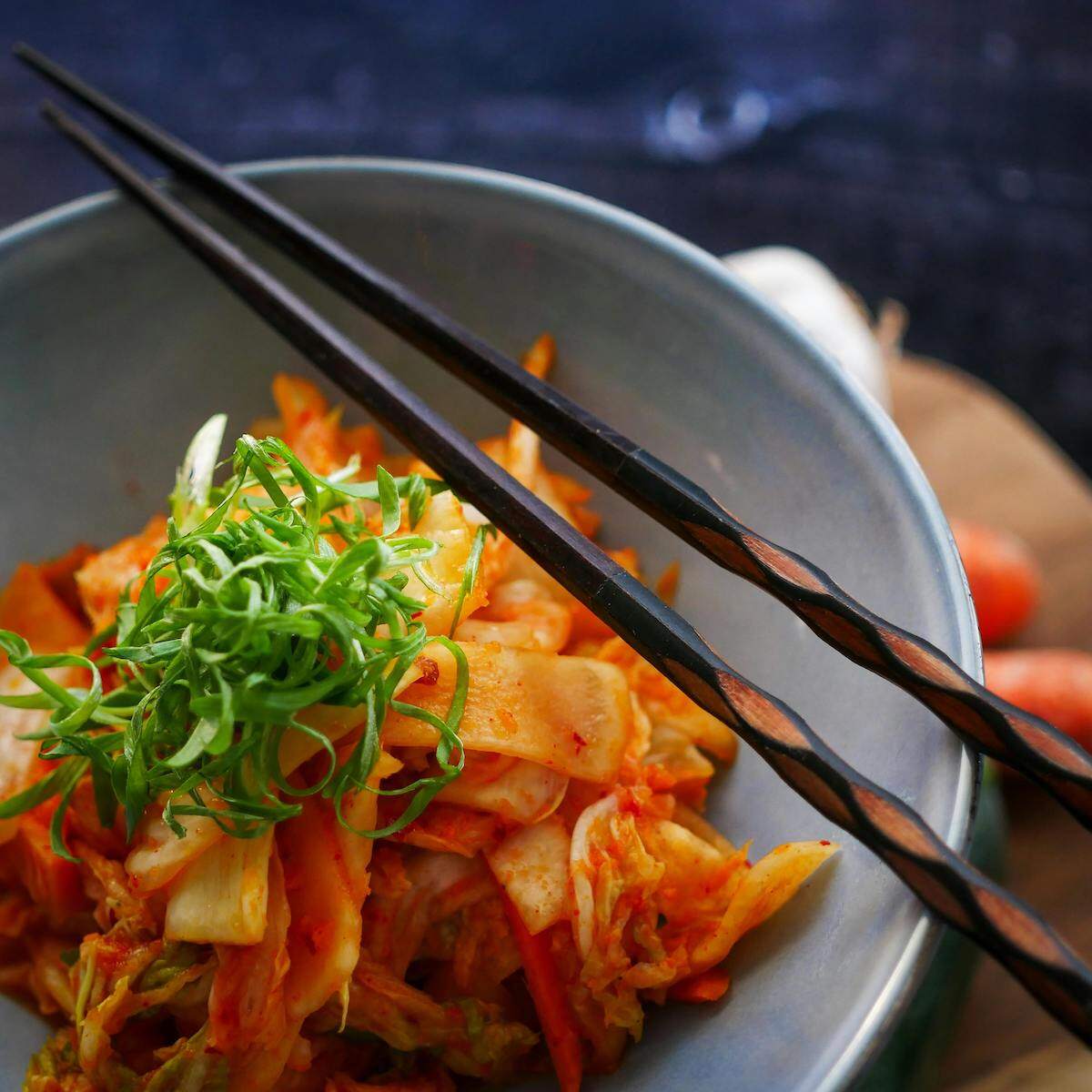 A bowl of vibrant kimchi, a spicy and flavorful vegetarian dish made from fermented vegetables, garnished with fresh green onions and served with chopsticks. This tasty dish can be found in Uzbekistan, adding to the diverse vegetarian options available.