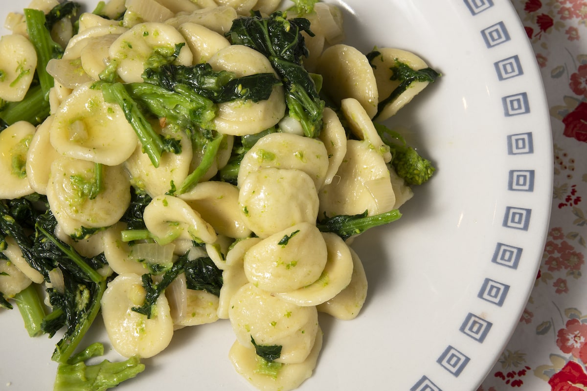 A plate of orecchiette con cime di rapa, a traditional southern Italian pasta dish made with turnip greens and olive oil, served in a white bowl with a geometric border.