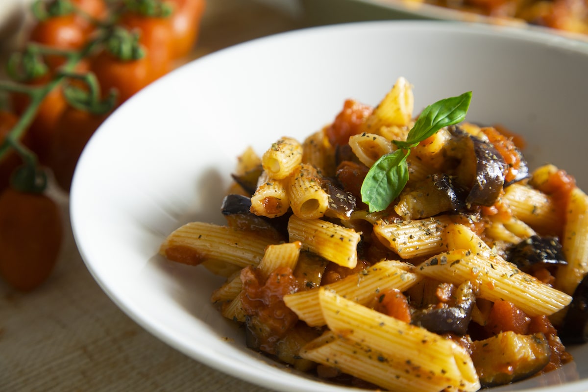A plate of orecchiette con cime di rapa, a traditional southern Italian pasta dish made with turnip greePasta alla Norma served in a white bowl, featuring penne with tomato sauce, fried eggplant, and fresh basil, a classic Sicilian vegan dish.