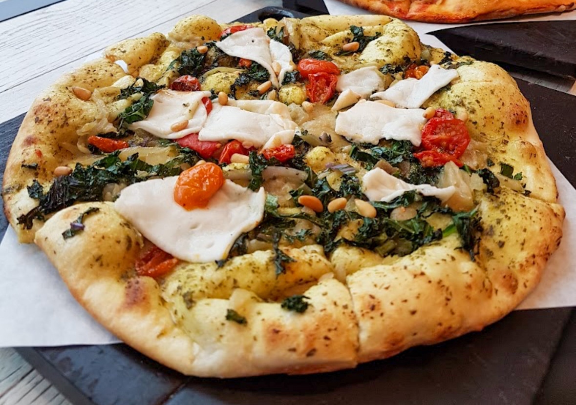 Vegan pesto pizza with tomatoes, greens, pine nuts, and nut cheese on a fluffy at Virtuous Pie in Vancouver