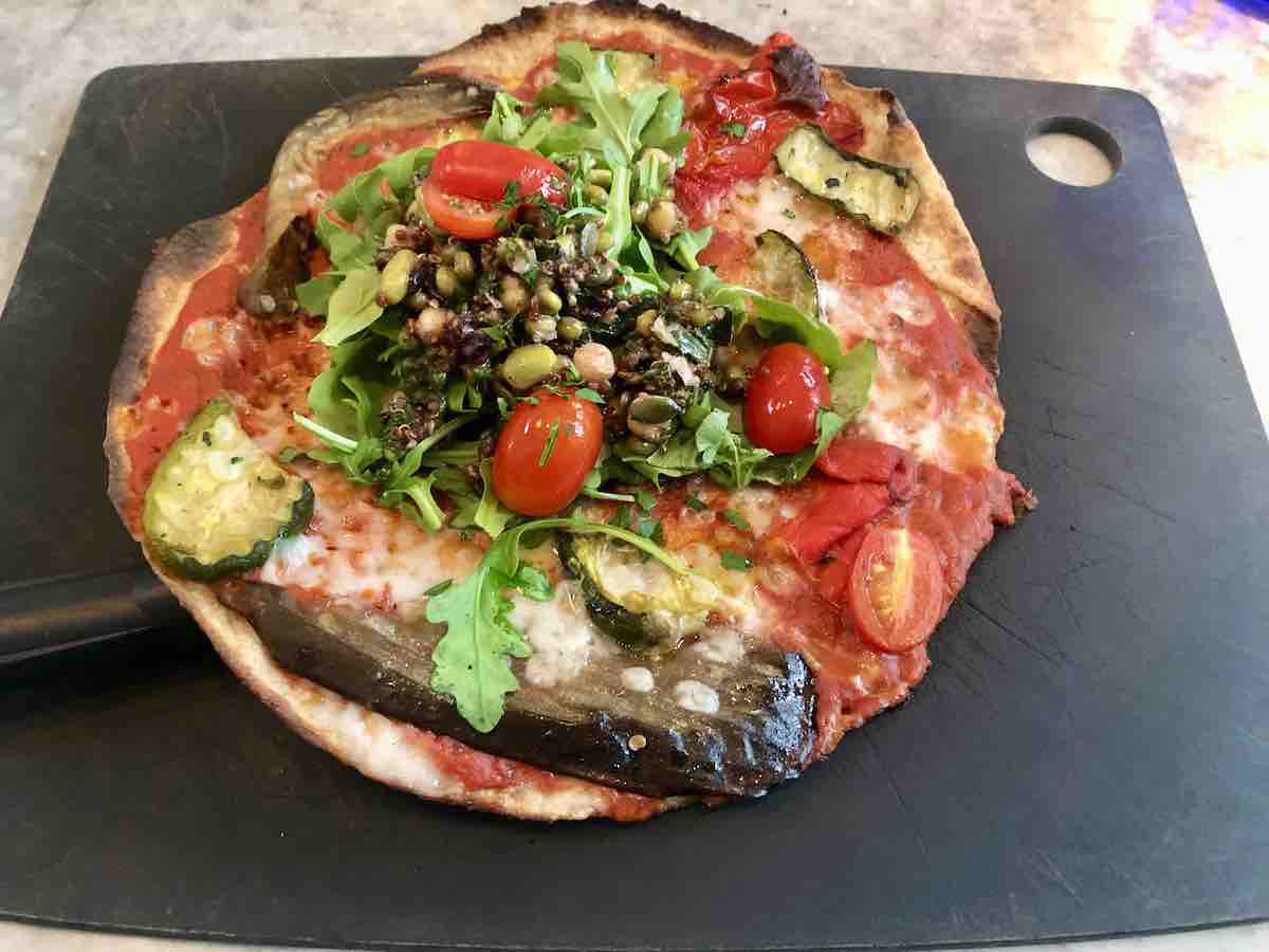Thin-crust vegan pizza from Purezza in Brighton, topped with tomato sauce, dairy-free cheese, grilled courgette, aubergine, cherry tomatoes, and a fresh arugula and lentil salad.