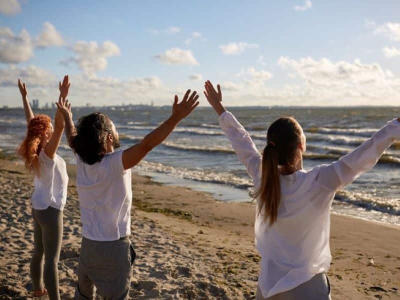 three people standing on the beach doing mountain pose during a vegan yoga retreat