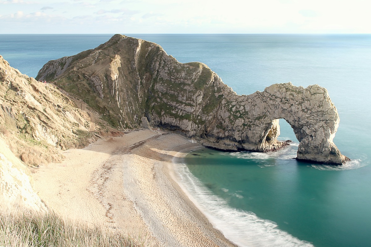 The iconic rock arch of Durdle Door on the Jurassic Coast, with turquoise waters and a sandy beach.