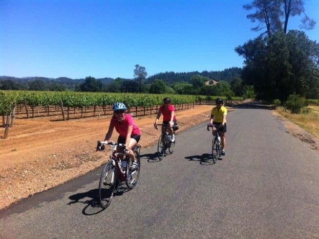three women cycling through vineyards in Healdsburg, California on a wine yoga retreat