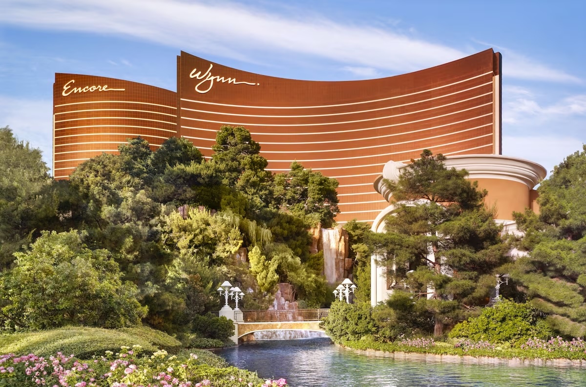 Exterior view of the Wynn and Encore resorts in Las Vegas, Nevada, surrounded by lush greenery, gardens, and a tranquil waterfall.