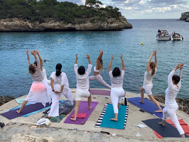 group of women wearing all white while standing in warrior one pose during a yoga retreat in Mallorca
