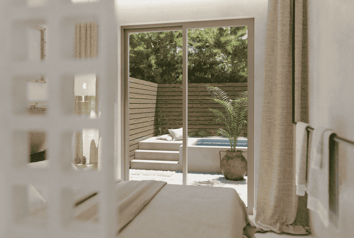 A tranquil bedroom at Açai Plant-Based Hotel with soft, neutral tones and a sliding glass door leading to a private outdoor plunge pool. The secluded patio is surrounded by lush greenery and a wooden privacy fence, creating a serene retreat for relaxation.